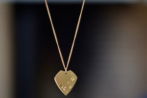 Petal Print Pick Necklace by Kaylin Hertel is a guitar pick shaped pendant with hand engraved petal motif, hanging on a 14k yellow gold chain. Handmade in Los Angeles.