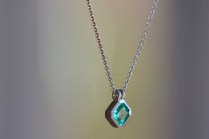 Side view of the The duo bale emerald pendant in platinum by Elizabeth Street is a bezel set Colombian emerald set on its axis in a double bale and on a platinum chain.