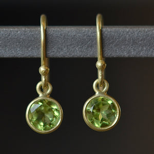 Tiny moon earrings by Tej Kothari are lightly faceted and translucent bezel set round and inverted stones on a gold ear wire hook in peridot.