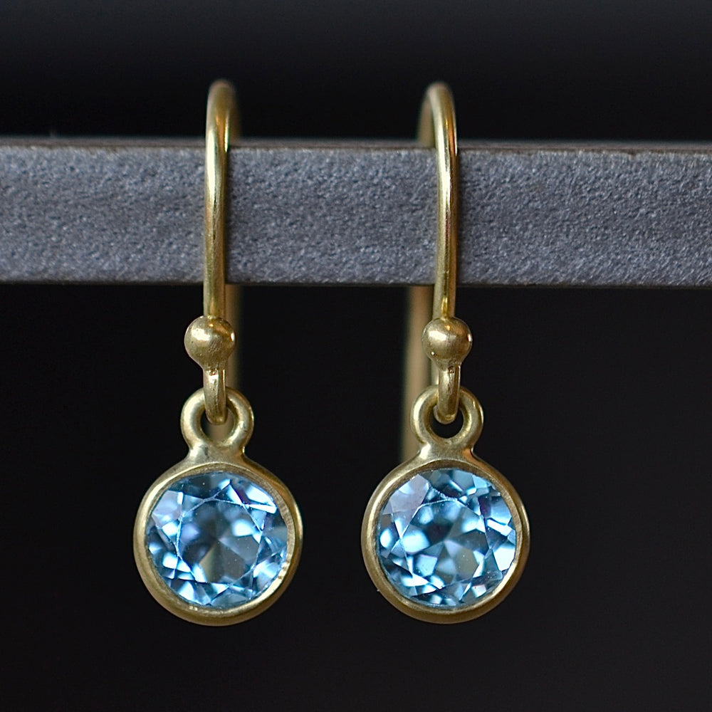 Tiny moon earrings by Tej Kothari are lightly faceted and translucent bezel set round and inverted stones on a gold ear wire hook in blue topaz.
