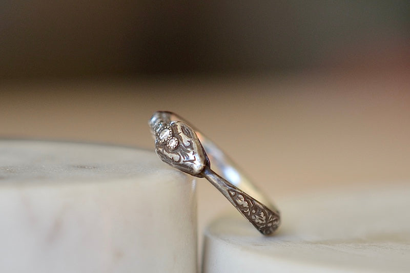 The Ouroboros Band by Arman Sarkyssian is a ring depicting a snake, swallowing its tail in oxidized silver with a half eternity diamond setting on its back. 