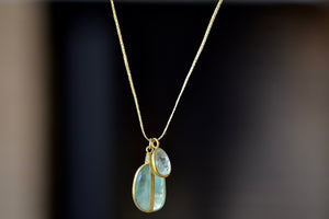 Banded Two Stone Necklace in Aquamarine by Pippa Small is a free form two stone pendant necklace of which one stone is banded and smooth and the other is bezel set and faceted on gold cord with gold seed charm.