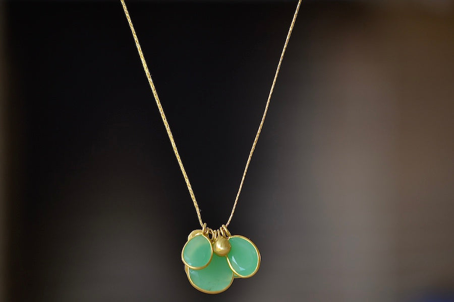 Colette Cluster Necklace in Chrysoprase with Gold Drops designed by Pippa Small is a Cluster of chrysoprase pendants bezel set stones in various sizes with two (2) 18k gold beads on 22" golden waxed cotton cord also known as the Flourishing Green necklace..
