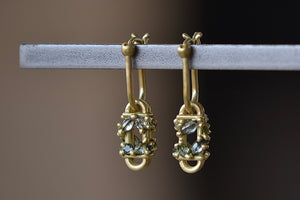 
            
                Load image into Gallery viewer, The Short Fontaine Bar Earrings in Green by Polly Wales from the side are A hinge lock hoop in 18k gold is attached to a rectangular box that has an encrusted vine of inverted green to gray mixed sapphires with matte gold dots.
            
        