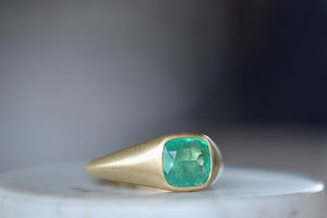 A signet ring in green emerald by Elizabeth street jewelry is a vivid cushion cut and lightly faceted Colombian emerald on a tapered band in 18k satin finish yellow gold. Handmade in Los Angeles.