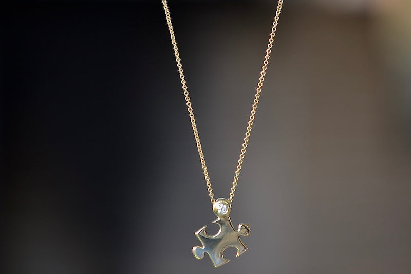 
            
                Load image into Gallery viewer, Mini Impetus Puzzle Piece Pendant by Retrouvai is a high polish puzzle piece in gold, accented with one white diamond hangs on a chain. Handcrafted in Los Angeles.
            
        