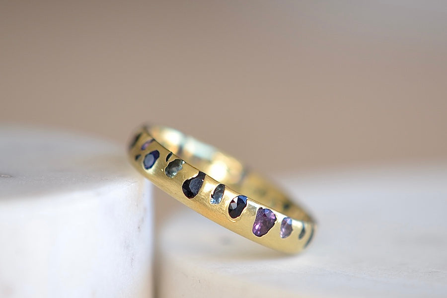 Tilted in sunlight Polly Wales Black with Teal, Purple, aqua and navy sapphires Confetti Band ring in size 7.5 that is Cast not Set.