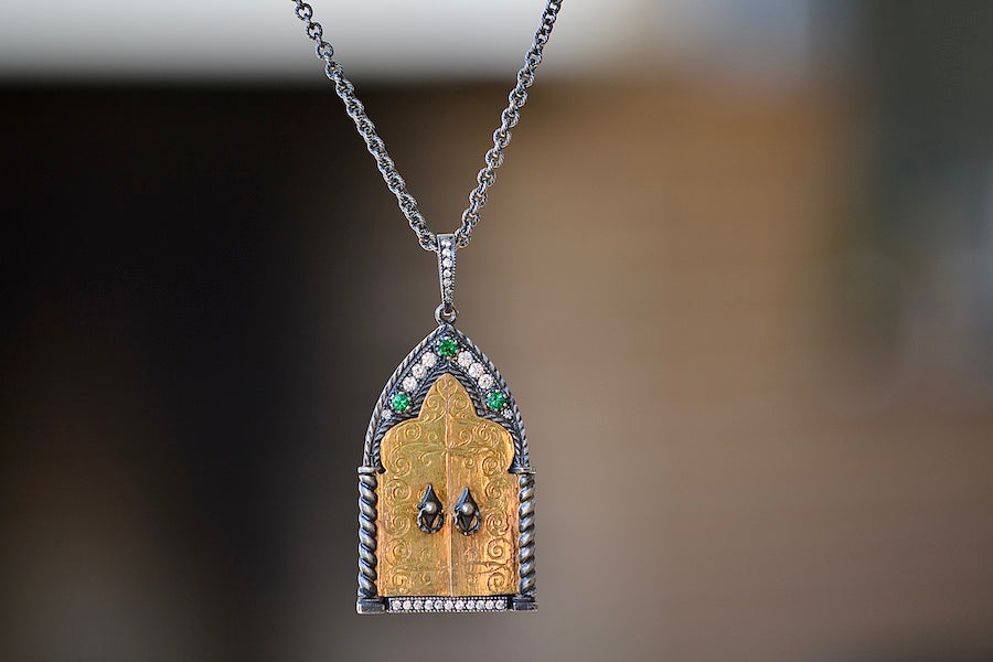 The Cathedral Door Locket by Arman Sarkyssian is a locket consisting of an oxidized silver back and gold door parts with three accent emeralds and eleven small round white diamonds on the bottom and six toward the top. The doors are 22k Yellow Gold and open and the pendant hangs off a silver ring with additional diamonds and on an Oxidized Sterling Silver Chain to form this Pendant Necklace.