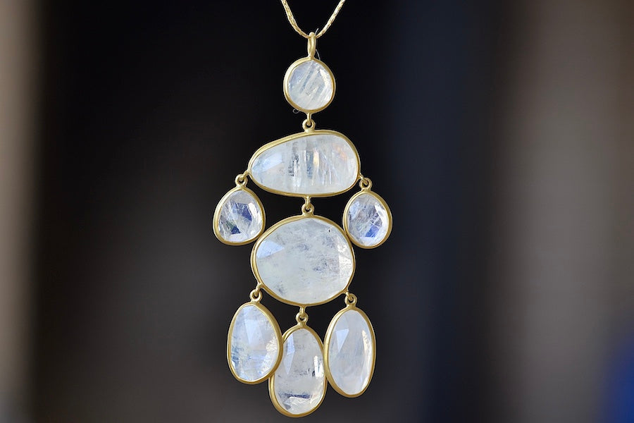 The Baroque Pendant in Moonstone and 18K by Pippa Small is Eight stones that are organically shaped, lightly faceted, translucent milky white and iridescent are arranged in a baroque pattern, all are bezel set in 18k yellow gold and attached with hooks to hang on a 24" golden waxed cotton cord to form this statement necklace.  