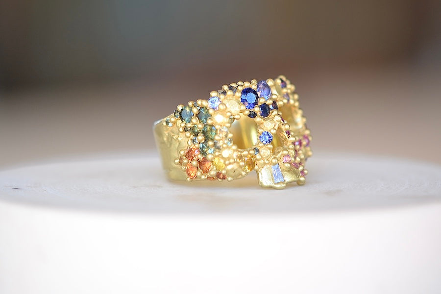 Encrusted River Skull Ring is a Polly Wales' classic squared 18k yellow gold small face skull ring, encrusted with gradated rainbow sapphires in her pebbles on a  river style and with one white diamond baguette snaggletooth. Recycled gold. Cast in Place. Cast not set size 7.5. Handmade in Los Angeles.