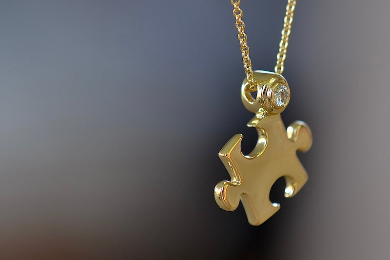 
            
                Load image into Gallery viewer, Mini Impetus Puzzle Piece Pendant by Retrouvai is a high polish puzzle piece in gold, accented with one white diamond hangs on a chain. Handcrafted in Los Angeles.
            
        