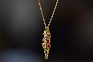 
            
                Load image into Gallery viewer, Side view of Vertical Fontaine Bar Necklace in Plum Blossom by Polly Wales is An oval and three dimensional bar in 18K yellow gold holds a vine of encrusted and inverted sapphires in pink, fuchsia and red that have been cast and are accompanied by matte gold dots. The bar hangs on a beautiful gold chain and bale.
            
        