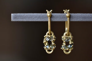 The Short Fontaine Bar Earrings in Green by Polly Wales are a hinge lock hoop in 18k gold is attached to a rectangular box that has an encrusted vine of inverted green to gray mixed sapphires with matte gold dots.