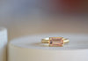 Elizabeth Street Jewelry Eagle Claw Bar ring in light pink peach tourmaline , clear and translucent, tourmaline is a radiant cut pink tourmaline in a four prong eagle claw east/west bezel setting on a 14k satin 3mm yellow gold band size 7..