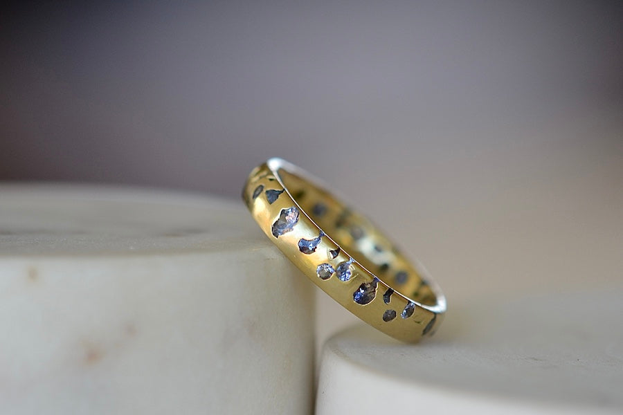 The Cornflower Blue Sapphire Confetti Band designed by Polly Wales is a narrow 18k yellow recycled gold wedding band/ring with speckled ombre light blue sapphires around the circumference. It is cast not set and handmade in Los Angeles.