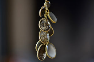 
            
                Load image into Gallery viewer, The Colette Set Cluster with Pyrite, Hematite, Tourmalated Quartz and Gray Moonstone Pendant Necklace is a cluster of nine bezel set, smooth or lightly faceted stones including Pyrite, Hematite, Tourmalated Quartz, and Gray Moonstone, all in 18k yellow gold on a 23&amp;quot; golden waxed cotton cord form this necklace. 
            
        
