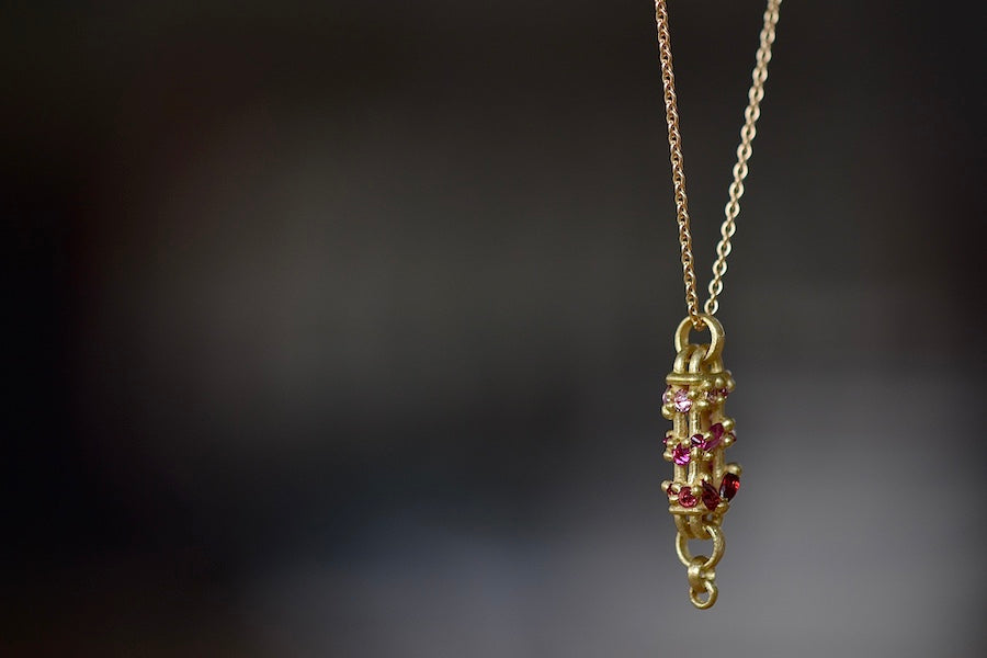 
            
                Load image into Gallery viewer, Details of stones and bar on Vertical Fontaine Bar Necklace in Plum Blossom by Polly Wales is An oval and three dimensional bar in 18K yellow gold holds a vine of encrusted and inverted sapphires in pink, fuchsia and red that have been cast and are accompanied by matte gold dots. The bar hangs on a beautiful gold chain and bale.
            
        
