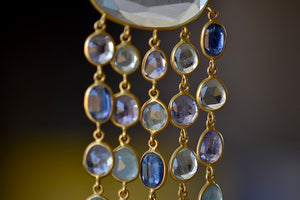 Raincloud Pendant Necklace by Pippa Small is a Large, faceted and transparent aquamarine with five rows of five stones each in blue to light purple hued tanzanite, aquamarine and kyanite bezel set stones in 18k yellow gold w extra long golden waxed cotton cord and accent bead for draping over head and no clasp.