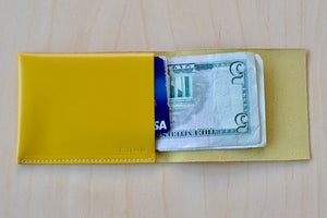 Simple Flap wallet in yellow leather and white stitching from architect Alice Park shown open with bills and cards.