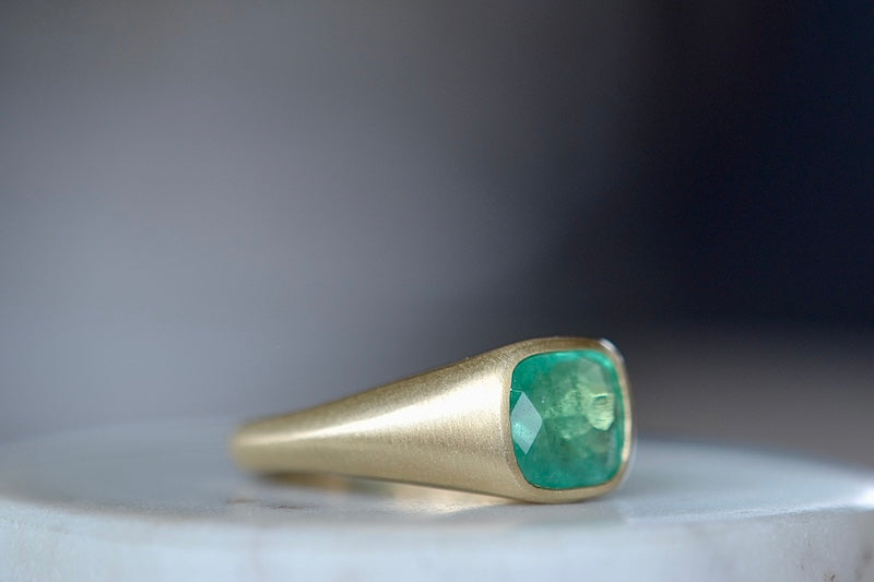 Side view of A signet ring in green emerald by Elizabeth street jewelry is a vivid cushion cut and lightly faceted Colombian emerald on a tapered band in 18k satin finish yellow gold. 
