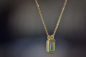 Side view of The Duo Bale Emerald Pendant Necklace by Elizabeth Street Jewelry Katie Finn is a bezel set rectangular and translucent shaped Columbian emerald on a double bale and on a 18k yellow gold chain. Perfect for layering or to wear as a solo piece. Handmade in Los Angeles.