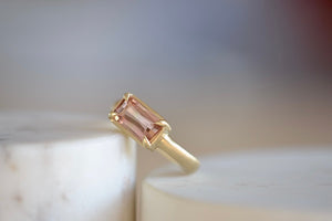 Elizabeth Street Jewelry Eagle Claw Bar ring in light pink peach tourmaline , clear and translucent, tourmaline is a radiant cut pink tourmaline in a four prong eagle claw east/west bezel setting on a 14k satin 3mm yellow gold band size 7..
