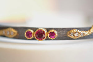 
            
                Load image into Gallery viewer, Arman Sarkysian Oxidized Snake Cuff with Ruby trio  is  shaped and hammered into a cuff that is adorned with two coiling gold snakes with diamonds six (6) three (3) each and three bezel set rubies with milgrain detail.
            
        