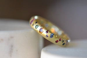 Tilted Polly Wales Classic Rainbow Confetti Band Ring in 18k recycled yellow gold with green, yellow, orange, blue, purple and pink sapphires and cast not set. Size 7.