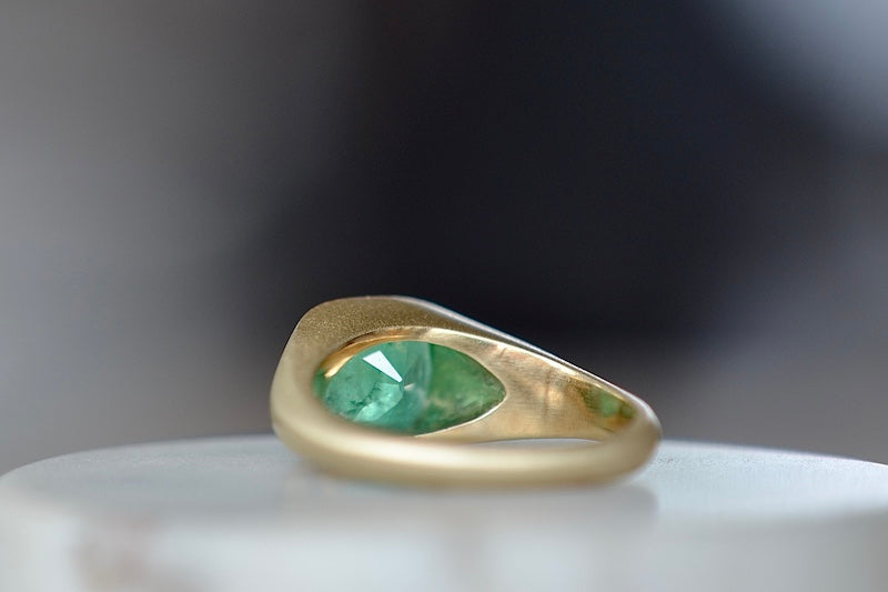 
            
                Load image into Gallery viewer, A signet ring in green emerald by Elizabeth street jewelry is a vivid cushion cut and lightly faceted Colombian emerald on a tapered band in 18k satin finish yellow gold. 
            
        