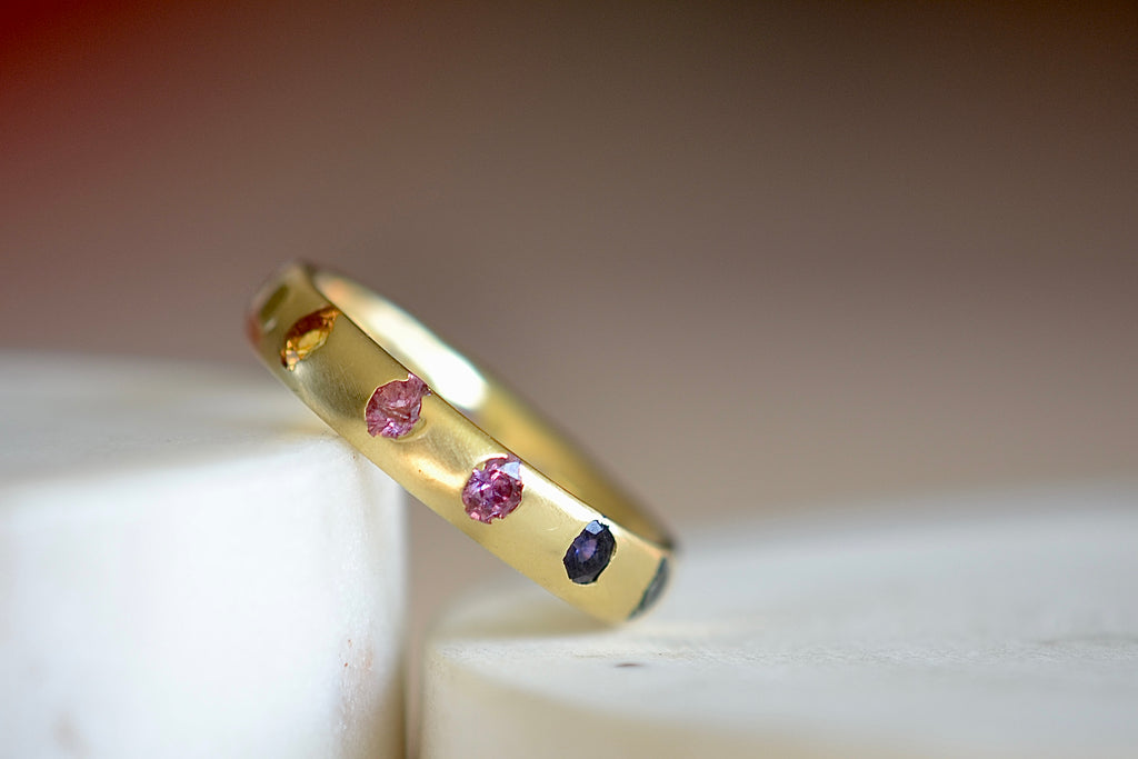 Celeste Ring in Blossom Crush by Polly Wales is a wide 18k recycled yellow gold band with sparkly rainbow sapphires in orange, yellow, green, pink, blue and purple peppered around the circumference. Recycled gold. Cast in Place. Cast not set. Handmade in Los Angeles.