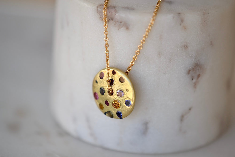 
            
                Load image into Gallery viewer, Polly Wales Spinning Disc Pendant Necklace in 18K yellow gold with scattered rainbow sapphires in orange, yellow, pink, blue, purple and lilac hangs on a beautiful chain 22&amp;quot; cast in place and cast not set in recycled gold.
            
        