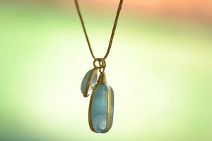 Banded Two Stone Necklace in Aquamarine by Pippa Small is a free form two stone pendant necklace of which one stone is banded and smooth and the other is bezel set and faceted on gold cord with gold seed charm.