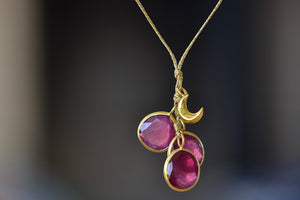 Close up of The Colette Set Cluster with Moon and Ruby Necklace is a  cluster of three bezel set and lightly faceted ruby stones, accompanied by a gold moon, all in 18k yellow gold on a 22" golden waxed cotton cord form this necklace. 