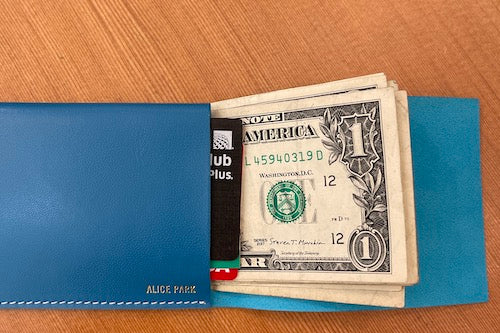 
            
                Load image into Gallery viewer, Simple Flap wallet in blue leather and white stitching from architect Alice Park shown open with bills and cards.
            
        