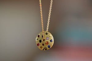 Polly Wales Spinning Disc Pendant Necklace in 18K yellow gold with scattered rainbow sapphires in orange, yellow, pink, blue, purple and lilac hangs on a beautiful chain 22" cast in place and cast not set in recycled gold. 