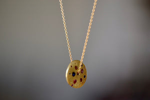 
            
                Load image into Gallery viewer, Polly Wales Spinning Disc Pendant Necklace in 18K yellow gold with scattered rainbow sapphires in orange, yellow, pink, blue, purple and lilac hangs on a beautiful chain 22&amp;quot; cast in place and cast not set in recycled gold.
            
        