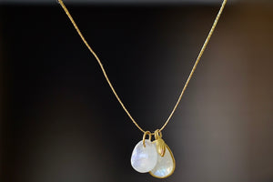 
            
                Load image into Gallery viewer, From the back. The Colette Drill Pendant with Seed Charm in Moonstone is a cluster of two milky white rainbow moonstones of which one is bezel set and lightly faceted and the other is smooth and round. These are accompanied by a sun bead, all in 18k yellow gold on a 20&amp;quot; golden waxed cotton cord form this necklace. 
            
        