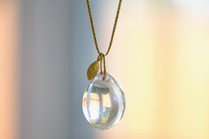 
            
                Load image into Gallery viewer, The Coconut Pendant with Seed Charm Necklace in Crystal  designed by Pippa Small is a One clear, transparent and smooth crystal stone with natural inclusions is drilled and hooked on to a gold loop, and accompanied by a bead in 18k yellow gold on a 24&amp;quot; golden waxed cotton cord form this necklace.
            
        