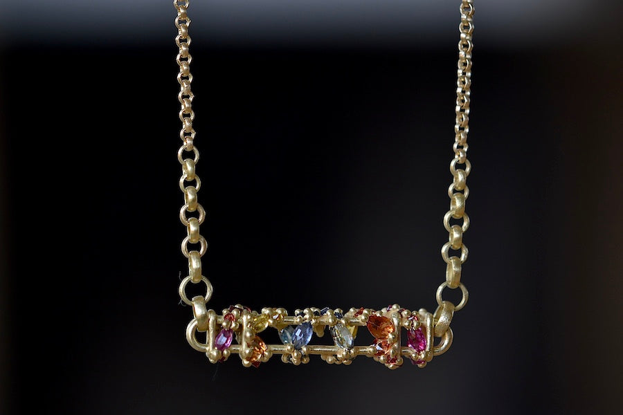 
            
                Load image into Gallery viewer, Back view of Horizontal Fontaine Bar Necklace in Rainbow by Polly Wales is An oval and three dimensional bar in 18K yellow gold holds a vine of encrusted and inverted rainbow sapphires in pink, fuchsia, blue, yellow, green and red that have been cast and are accompanied by matte gold dots. Recycled Gold. Cast Not Set. Handmade in Los Angeles.
            
        